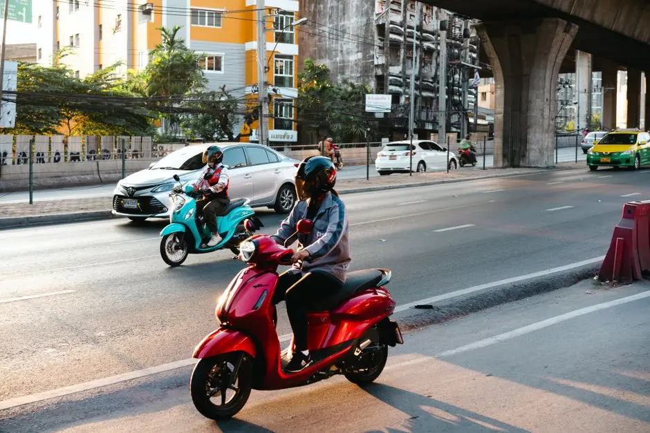 Two Riders On Scooters Navigate Through Bustling Streets Of Bangkok Th